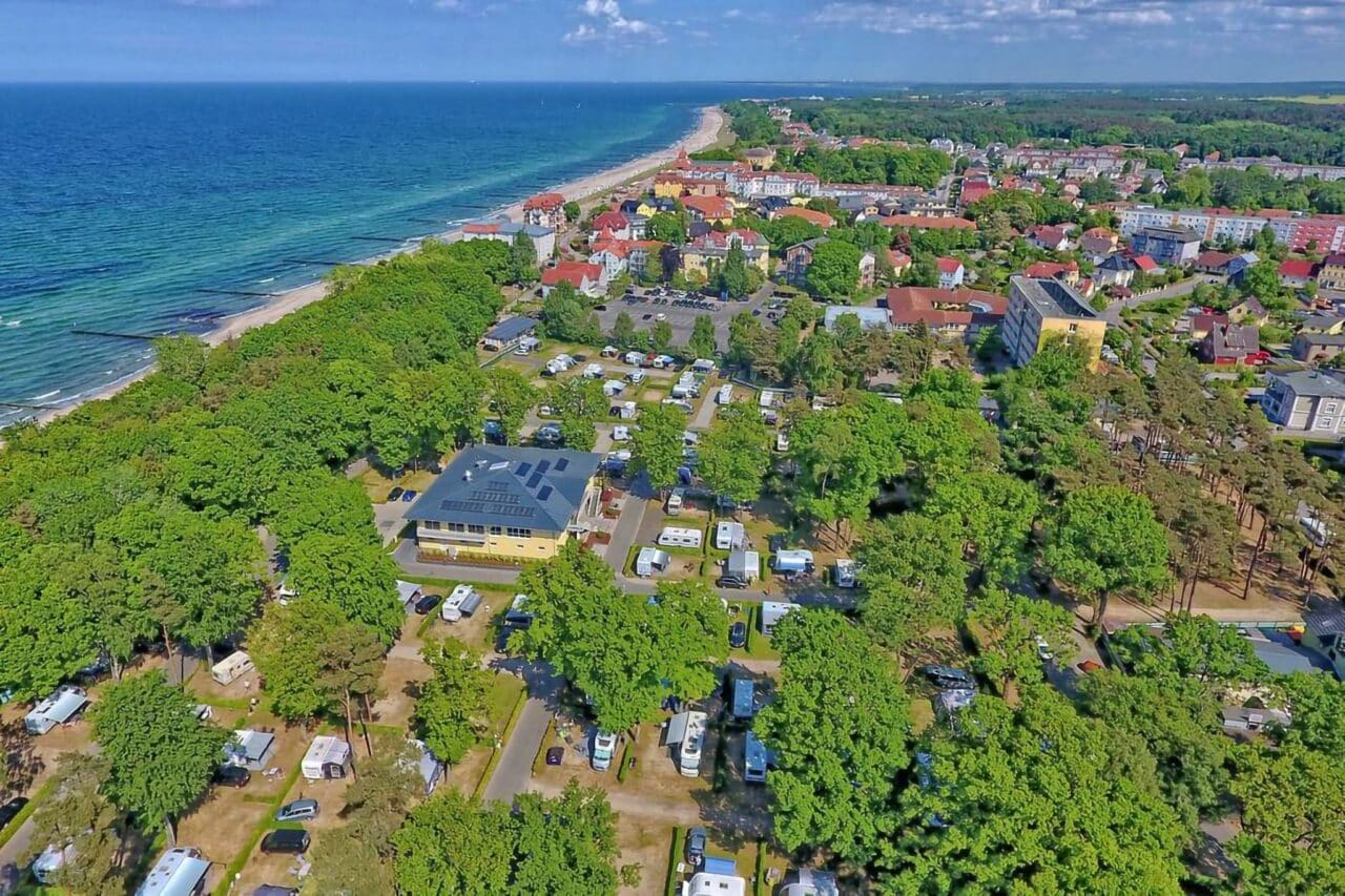 Camping.info nr 1 w Niemczech: Kemping Kühlungsborn. Możesz zobaczyć widok z lotu ptaka na kemping na wsi, z morzem w tle. 