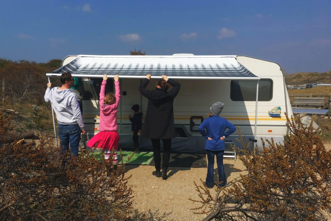 Checkliste: Camping mit Kind - Familie steht vor Wohnwagen mit Markise auf Campingplatz